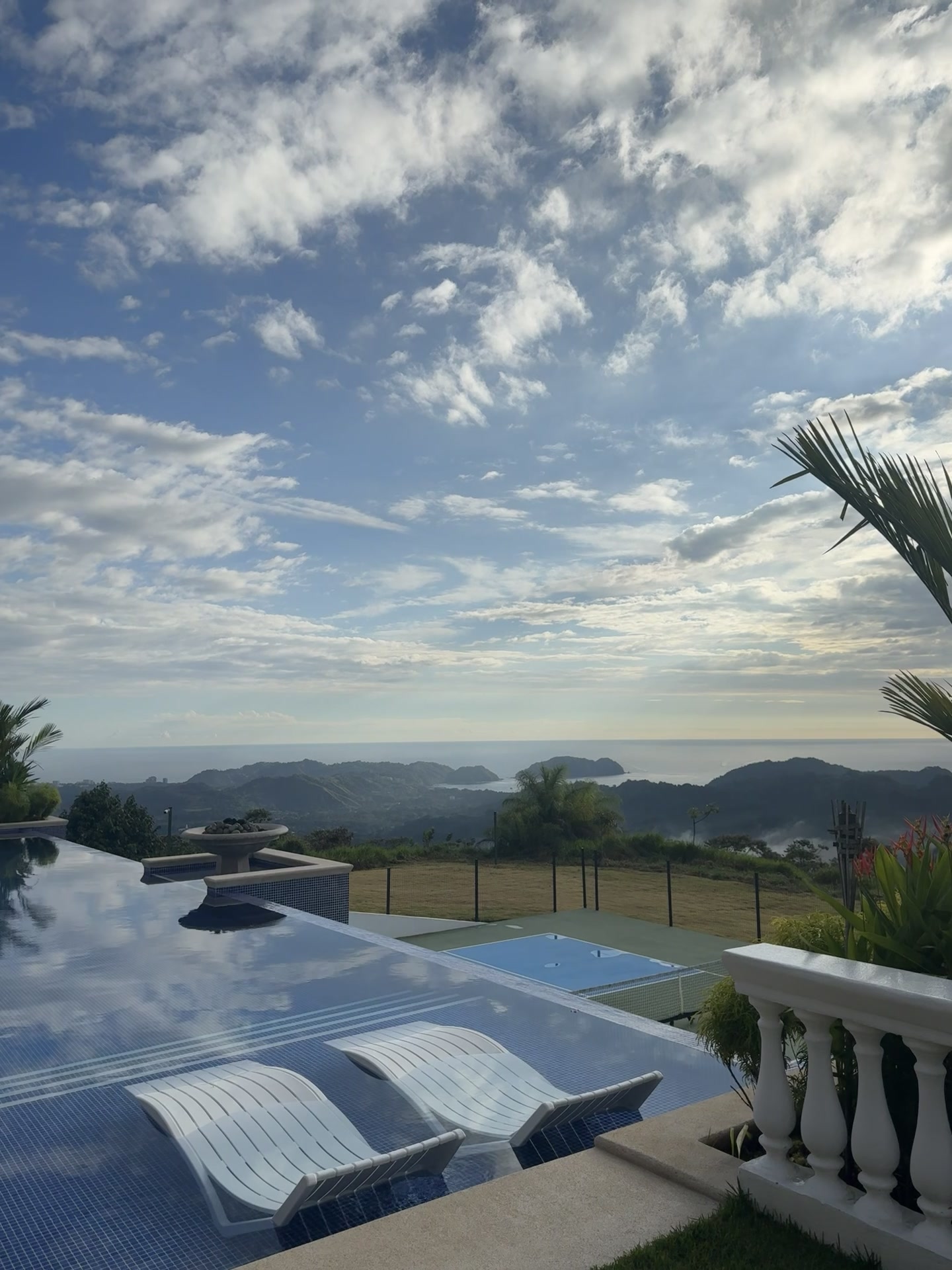 Pool panorama with ocean, mountains, and lounge chairs